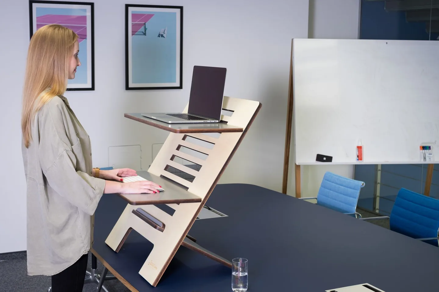 Nő állva dolgozik egy megemelt laptopos munkaállomásnál.